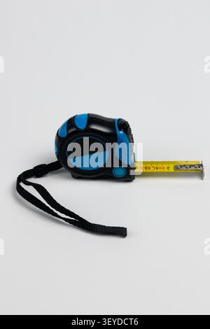 Hochauflösendes Studiofoto eines blau-schwarzen Maßbandwerkzeugs mit gelbem Band teilweise nach rechts verlängert. Das kompakte ergonomische Stockfoto