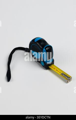 Hochauflösendes Studiofoto eines blau-schwarzen Maßbandwerkzeugs mit gelbem Band teilweise nach rechts verlängert. Das kompakte ergonomische Stockfoto