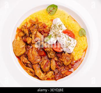 Herzhafter Hähncheneintopf mit cremiger Polenta, frischen Tomaten und zerbröckeltem Fetakäse Stockfoto