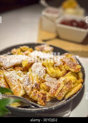 Berühmtes österreichisches Süßgericht Kaiserschmarrn, serviert in einer Pfanne mit Eis, Himbeere und gedünsteten Pflaumen Stockfoto