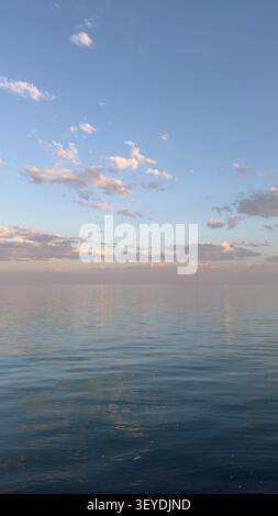 Sanfter pastellfarbener Sonnenuntergang über ruhigem Meer mit Wolkenreflexen Stockfoto
