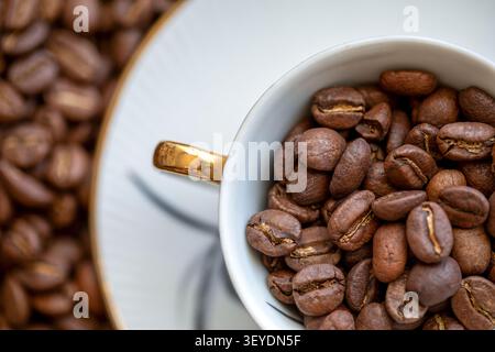 Eine Kaffeetasse mit Kaffeebohnen im Inneren und über den Tisch verteilt Stockfoto