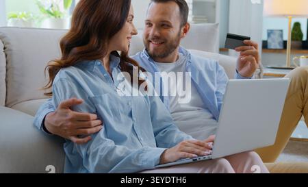 Glücklich lächelnde kaukasische Familie Shopping mit Laptop- und Kreditkartenkauf online mit einfachem Bankservice Lächeln umarmen sich zu Hause Mann mit Stockfoto