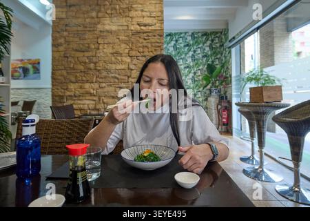 Nahaufnahme einer Frau, die Algensalat mit Essstäbchen in einem Restaurant isst. Gesunde Mahlzeit und natürliches Essen Moment. Stockfoto