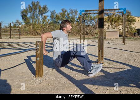 Mann, der Trizepsdips an Metallstäben während des Workouts im Freien durchführt. Stockfoto