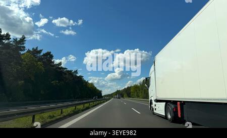 Weißer Lieferwagen, der auf einer Autobahn fährt, umgeben von grünen Bäumen und blauem Himmel mit flauschigen Wolken Stockfoto