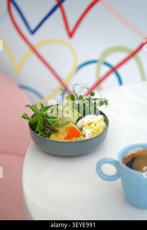 Frische Salatschale mit Avocado, Gemüse, pochiertem Ei und Kaffee auf weißem Tisch Stockfoto