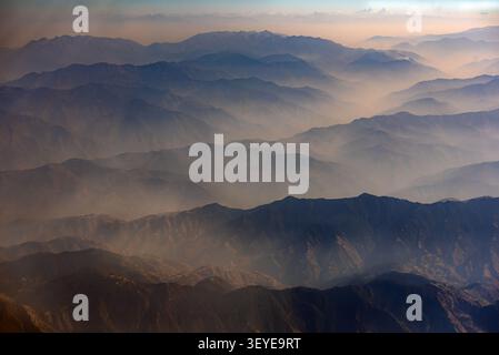Aus der Vogelperspektive auf die majestätische Himalaya-Bergkette mit mehrschichtigen Gipfeln, die unter einem sanften Licht in Kaschmir, Kaschmir, Pakistan in den nebeligen Horizont eintauchen Stockfoto