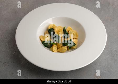 Ravioli mit Spinat in breiter weißer Schüssel auf grauem Steintisch, Blick von oben Stockfoto