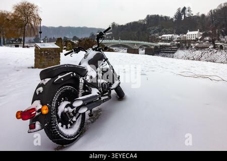 Eine Rückansicht eines Motorrads, das am Rand einer öffentlichen Straße geparkt ist, die mit einer dicken Schicht frischem Winter Schnee bedeckt ist Stockfoto