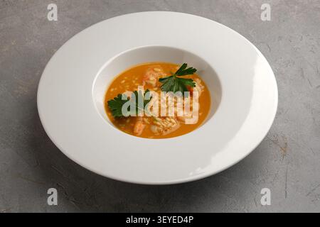 Reissuppe mit Meeresfrüchten, Garnelen und Petersilie, serviert in einer breiten weißen Schüssel auf grauer Steinoberfläche Stockfoto