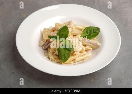 Cremige Penne-Pasta mit Basilikumblättern, geriebenem Käse, Pilzen und zartem Huhn in einer weißen Schüssel Stockfoto