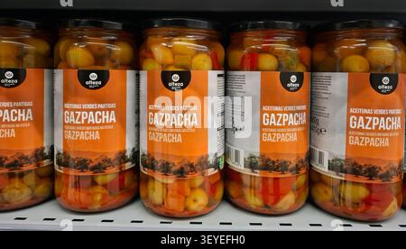 DENIA, SPANIEN, 15. November 2025. Gläser mit gesalzenen Oliven, gemischt mit bunten Gemüse, sind ordentlich im Supermarktregal in Spanien angeordnet. Diese Auswahl Stockfoto