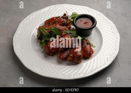 Glasierte Hähnchenflügel mit Sesamsamen, Koriander und Dippsoße auf weißem Teller Stockfoto