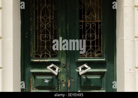 Nahaufnahme einer alten grünen Holztür mit kunstvollen schmiedeeisernen Gittern, abblätternder Farbe und Vintage-architektonischen Details. Eine zeitlose Stadt Stockfoto