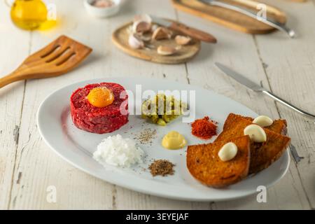 Rindertatar auf einem weißen Teller mit Eigelb, Toast, Gurken und Gewürzen Stockfoto