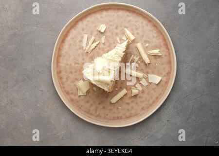 Scheibe weißer Schokoladenkuchen auf Keramikplatte mit verstreuten Spänen über Steinhintergrund Stockfoto