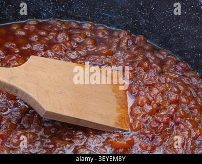 Hausgemachte gelbe Kirschmarmelade, die in einem Kochtopf mit Holzspachtel während der traditionellen Zubereitung von Obstkonserven und der saisonalen Konservierung kocht. Stockfoto
