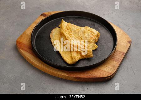 Goldenes Omelett in gusseiserner Pfanne auf Holzbrett über rustikaler Steinoberfläche serviert Stockfoto