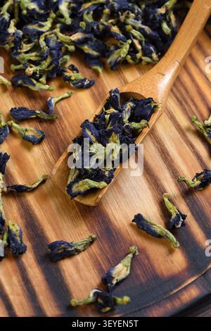 Ein Blick von oben auf getrocknete blaue Dornblüten (Clitoria ternatea) auf einem Holzteller mit einem gefüllten Holzlöffel. Ein Bio-pflanzlicher Inhaltsstoff für gesundes Blau Stockfoto