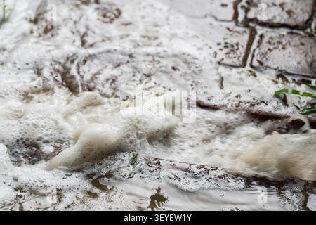 Schnell fließendes Regenwasser mit Schaum, der nach starkem Regen durch einen städtischen Sturmabfluss fließt. Konzept von Regenwasserabfluss, Entwässerung, Hochwasserprävention Stockfoto