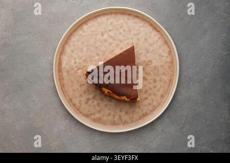 Eine Scheibe Schokoladen-Käsekuchen auf strukturierter Keramikplatte über grauem Steinhintergrund Stockfoto