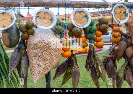 Marktstand im Freien, an dem frische Produkte wie hängende Avocados, Kürbis, Mais auf dem Kolben, Wurzelgemüse und eine große Tüte getrockneten Kaffees angeboten werden Stockfoto