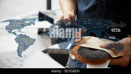 Mittealter Asiate hält Mohnpastry, hebt Telefon, tippt, zeigt HUD-Karten-Daten an Stockfoto