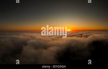 Die Sonne geht über einer riesigen Wolkendecke auf und erzeugt ein warmes Leuchten und einen atemberaubenden Blick aus der Luft Stockfoto