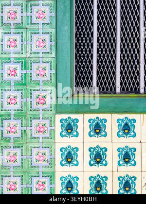 Detail traditioneller Peranakan-Keramikfliesen & grüßer Holzfensterrahmen mit Metallgitter an einer historischen Fassade in Malaysia Stockfoto