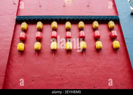 Reihen von gelben und roten traditionellen Laternen, die an einer strukturierten roten Wand hängen Stockfoto