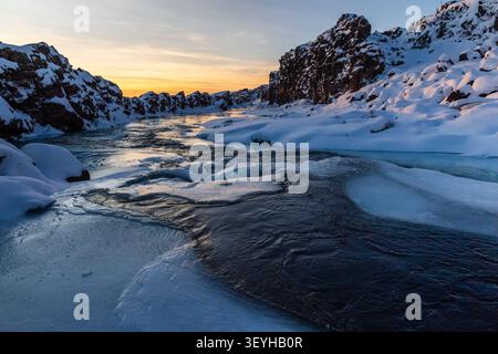 Winterszene im Freien mit einem schneebedeckten Fluss in der Nähe des teilweise gefrorenen Oxararfoss Wasserfalls im Thingvellir Nationalpark im Goldenen Kreis in Island. Stockfoto