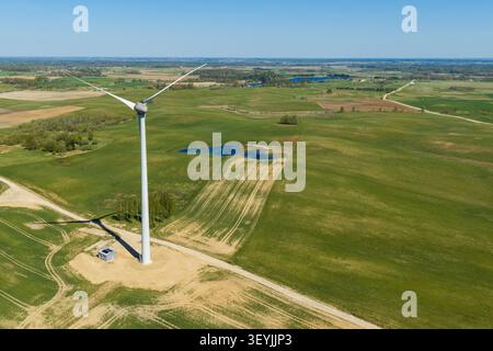 Aus der Vogelperspektive einer Windturbine in einem riesigen grünen Feld mit kleinen Teichen und einer unbefestigten Straße in der ländlichen Landschaft von Jacionys, Vilnius County, Lith Stockfoto