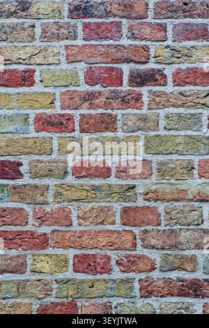 Mehrfarbige Ziegelwand im Vollrahmen mit roten, gelben und grauen Ziegeln und sichtbaren alten Mörtelfugen. Stockfoto