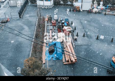 Hochwinkel-Ansicht von oben über Baumaterialien und Ausrüstung, die während des Schneefalls auf einem offenen Gelände in Tokio gelagert sind Stockfoto