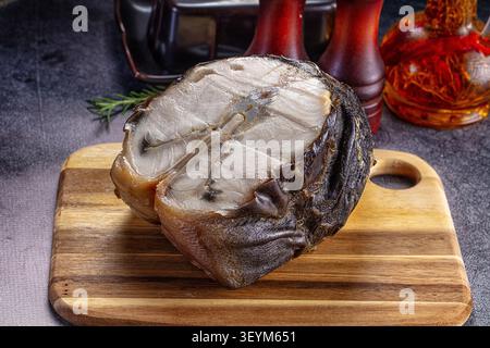 Geräuchertes Störfilet in Scheiben geschnitten, das das Innere in weiß auf Holzbrett freigibt. Dunkel verkohlte Haut steht im Kontrast zu blassem Fleisch. Rosmarinzweig, Pfeffer Stockfoto