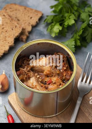 Geschmorte geräucherte Hähnchenflügel mit Gemüse und Gewürzen in einer offenen Dose auf einem Holzbrett, mit Roggenbrot, Petersilie, Knoblauch und Chili-Pfeffer Stockfoto