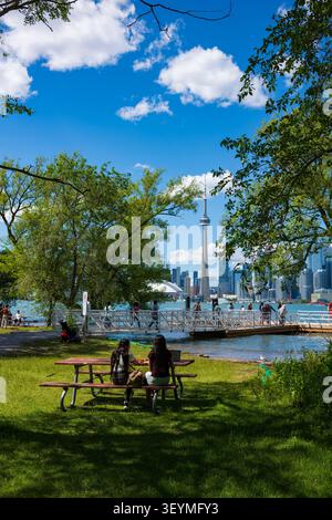 Toronto, Ontario, Kanada - 20. Juni 2026: Zwei Frauen sitzen an einem Picknicktisch und essen mit der Skyline von Toronto im Hintergrund zu Mittag Stockfoto