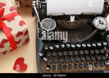 Vintage Schreibmaschine, Geschenkbox und Papierherz für Valentinstag auf beigefarbenem Hintergrund, Großaufnahme Stockfoto