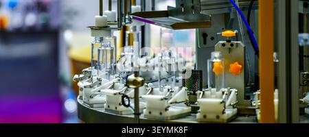 Industrielle automatisierte Maschinenlinie, die klare kosmetische Serumflaschen in Produktionsanlagen umsetzt Stockfoto