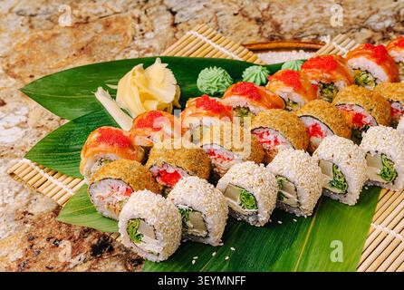 Eine farbenfrohe Sushi-Platte zeigt eine Vielzahl von Sushi-Brötchen, die ordentlich auf einem Holzbrett angeordnet sind. Zu den Garnituren gehören Ingwerscheiben und cremige grüne Gewürze, die frische Akzente verleihen. Stockfoto