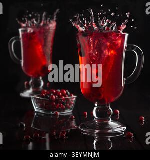 Leuchtend roter Glühwein mit Beeren und Spritzer in zwei Glasweingläsern im schwarzen dunklen Innenraum, quadratisch. - Fotomontage Stockfoto