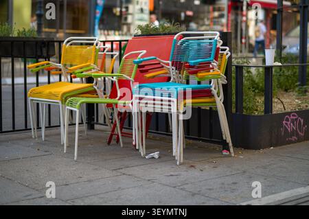 Die Angestellten haben diese lebhaften Caféstühle neben einen roten Tisch gestapelt. Diese aufgeräumte Anordnung entfernt den Bürgersteig und signalisiert, dass der Sitzbereich im Freien ist Stockfoto