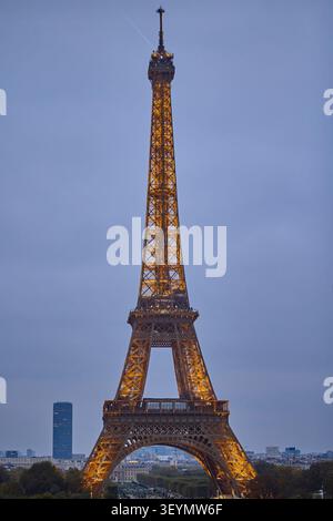 Der Eiffelturm leuchtet bei Sonnenuntergang unter einem bewölkten Himmel in goldenen Lichtern und symbolisiert Pariser Romantik und Eleganz. Stockfoto