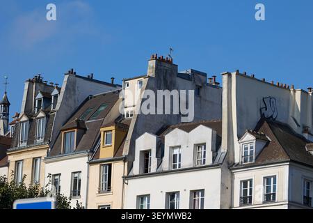 Aus nächster Nähe sehen Sie alte Pariser Wohngebäude mit schrägen Dächern, Dachfenstern und roten Schornsteinen unter klarem blauem Himmel. Stockfoto