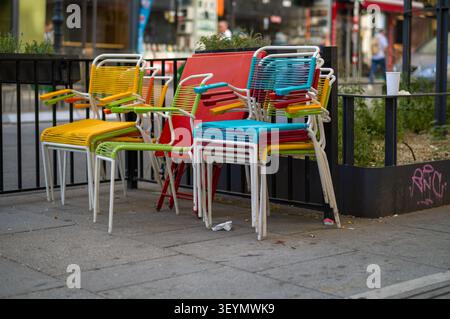 Die Angestellten haben diese lebhaften Caféstühle neben einen roten Tisch gestapelt. Diese aufgeräumte Anordnung entfernt den Bürgersteig und signalisiert, dass der Sitzbereich im Freien ist Stockfoto