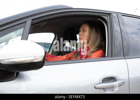 Fahrer sitzt tagsüber im Auto und blickt auf dem Parkplatz nach vorne. Aktivität findet tagsüber statt. Horizontal. Stockfoto
