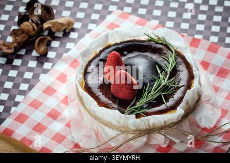 Ein baskischer Käsekuchen mit Erdbeere und Rosmarin, serviert auf einem Gericht mit zerknittertem Papier Stockfoto