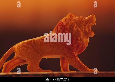 Close-up-Studio-Aufnahme einer orangefarbenen 3D-gedruckten Plastik-Löwenfigur, die vor einem stimmungsvollen bernsteinfarbenen Hintergrund brüllt. Stockfoto