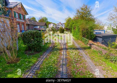 Rosdorf, Deutschland - 15. April 2026: Miniaturbahngleise auf grünem Gras mit Gänseblümchen vor dem historischen Bahnhofsgebäude in Rosdorf, Deutschland Stockfoto